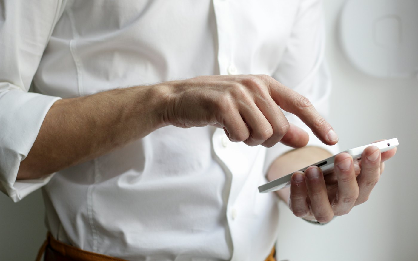 Beyaz gömlekli bir kişi akıllı telefonuna dokunuyor